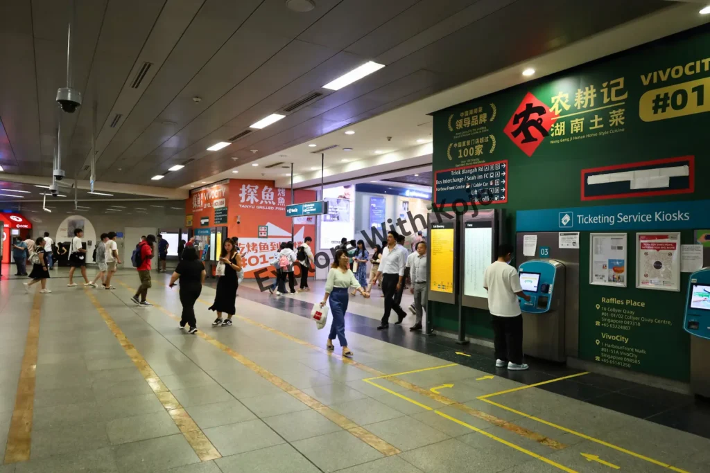 Commuters using ticketing kiosks and walking through VivoCity MRT station in Singapore.