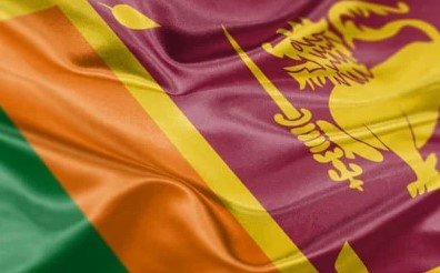 Flag of Sri Lanka with golden field, lion holding sword, and orange and green stripes.