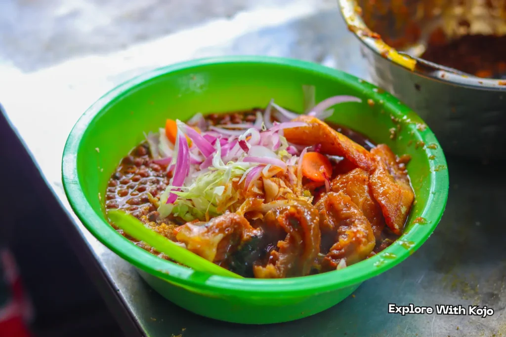 Traditional Ghanaian Aduwa served with ripe plantain, onions, and vegetables in a green bowl.