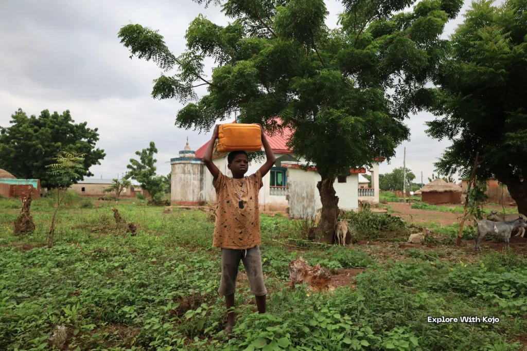 Child carrying water container on their head in the village.