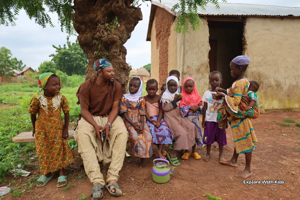 Children and a man sitting together in a village setting.