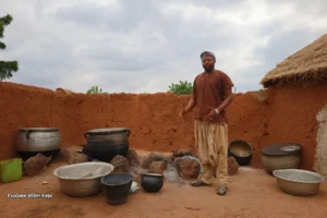 Man standing beside large African cooking pots.