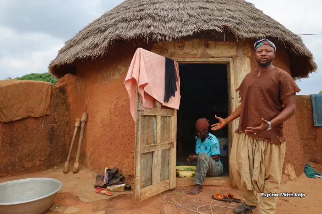 Family standing outside a round mud hut with thatched roof.