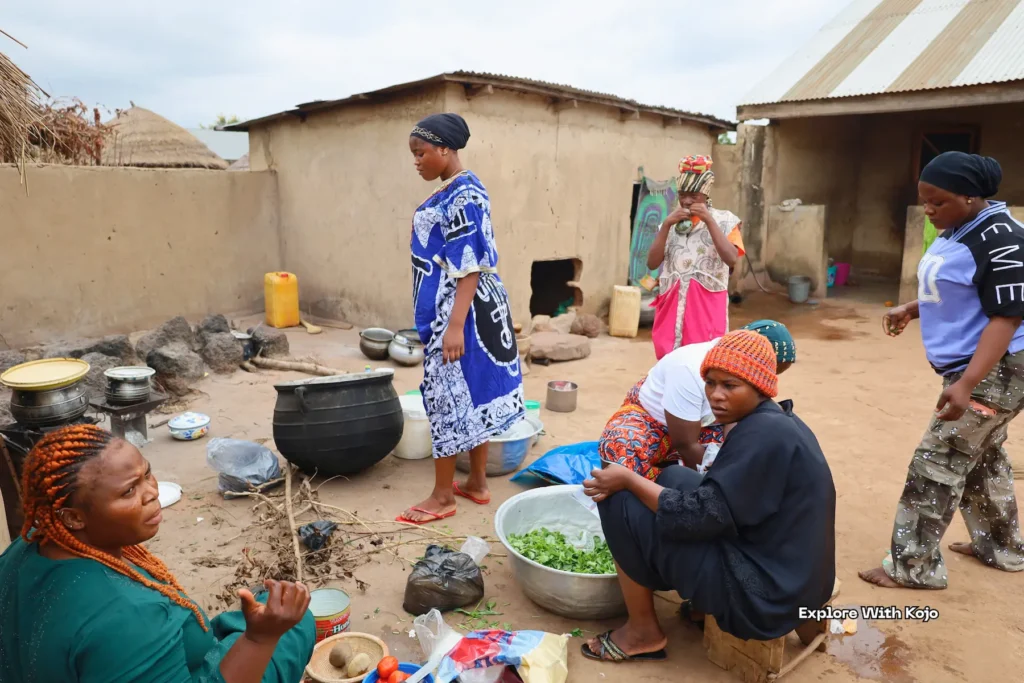 Women preparing food outdoors in a village compound.