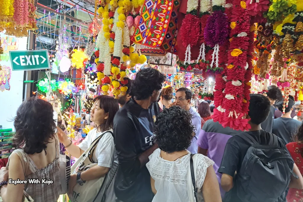 People browsing Deepavali stalls decorated with bright flowers and glowing lamps in Singapore.