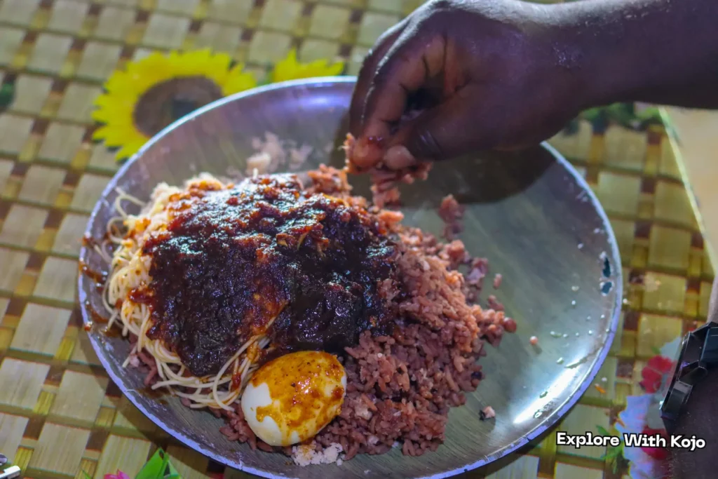 A person eating waakye with their hand from a metal plate.