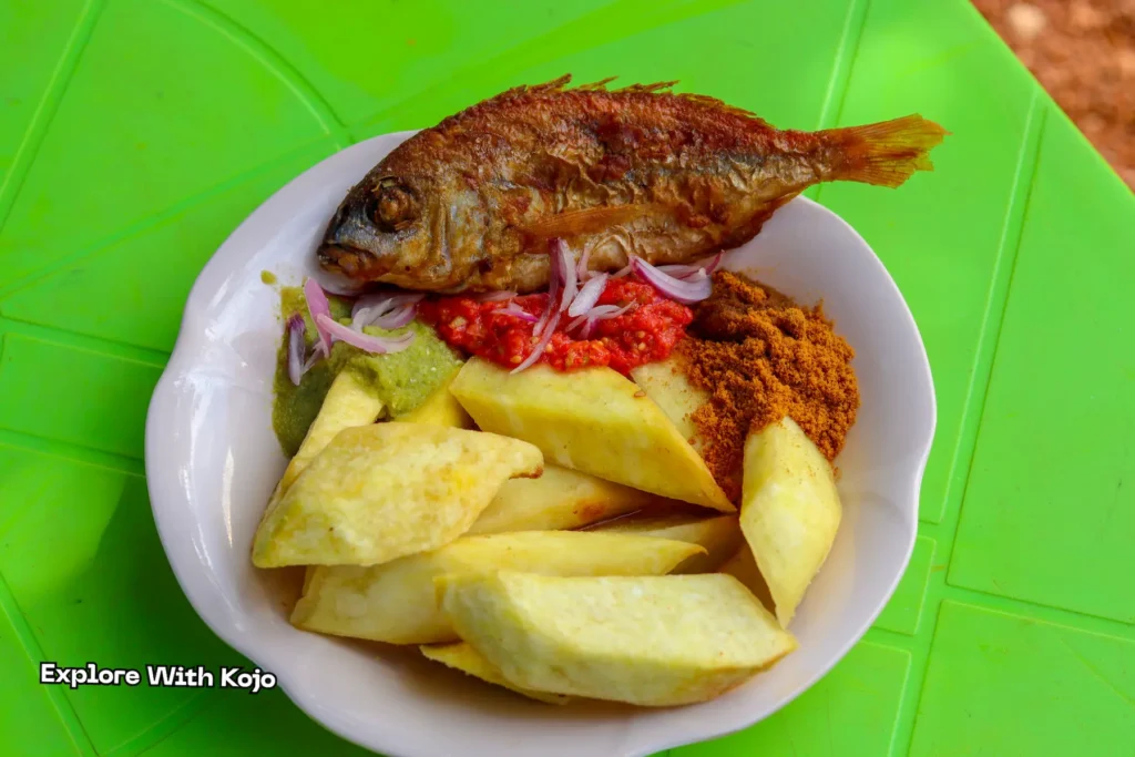 Fried fish with yam and spicy red pepper sauce served on a white plate.