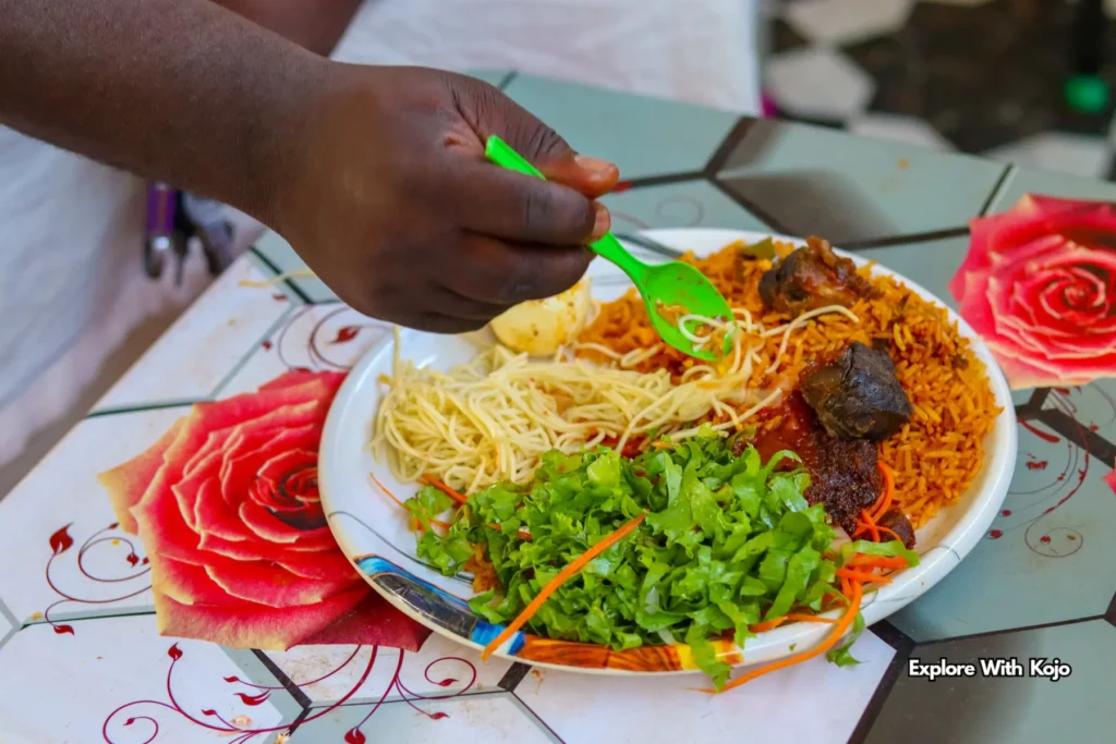 Person eating Ghana jollof rice with salad, spaghetti, and meat
