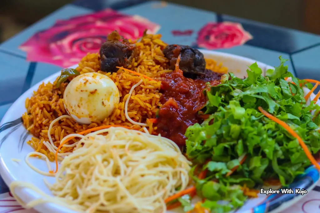 Plate of Ghanaian jollof rice served with egg, salad, and spaghetti