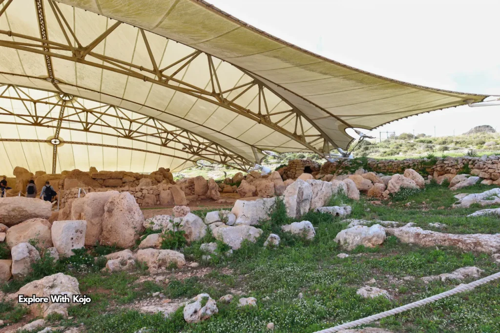 wide view of Ħaġar Qim canopy structure sheltering ancient stones with green grass around