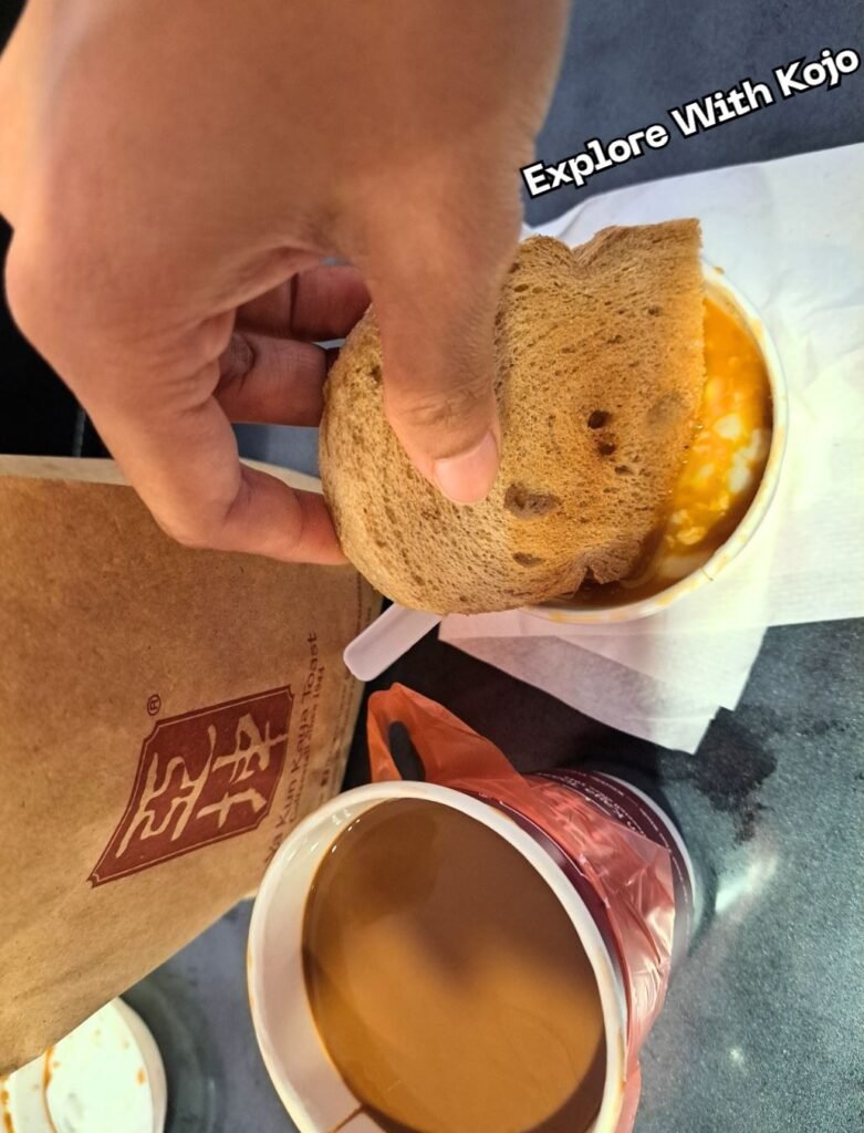 Hand dipping kaya toast into soft-boiled eggs during breakfast in Singapore