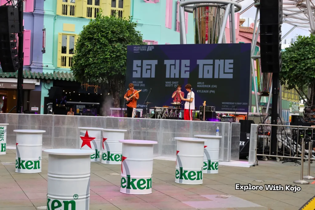 A live band performing on stage at Clarke Quay surrounded by colorful shophouses and Heineken-branded decor.
