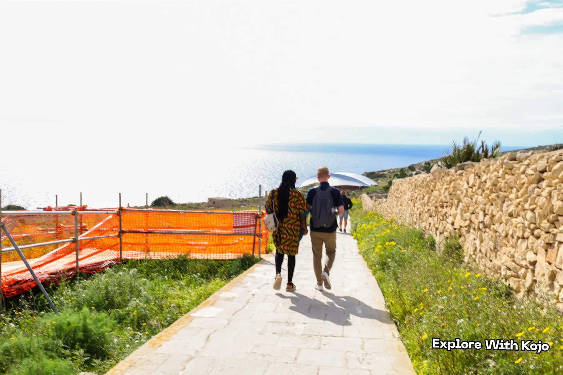 Couple walking down the stone path to Mnajdra Temple in Malta with a view of the Mediterranean Sea.