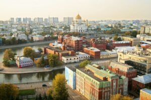 Aerial view of Moscow showing colorful historic buildings, the Moskva River, and the Cathedral of Christ the Saviour in the distance.