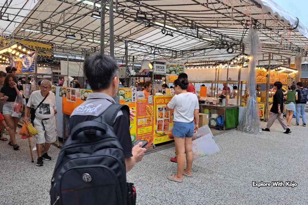 Daytime crowd at a Singapore Pasar Malam with multiple street food kiosks.