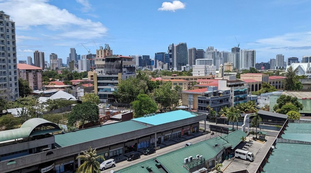 View of Manila city skyline with modern high-rises and low-rise neighborhoods under clear blue skies.