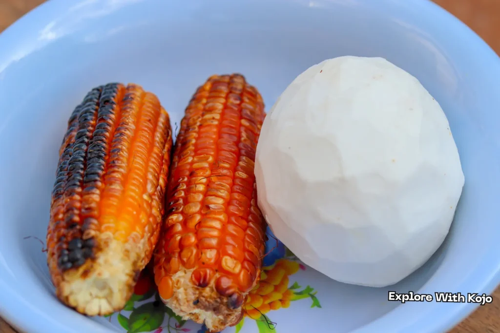 Roasted corn served with a peeled coconut in a bowl.