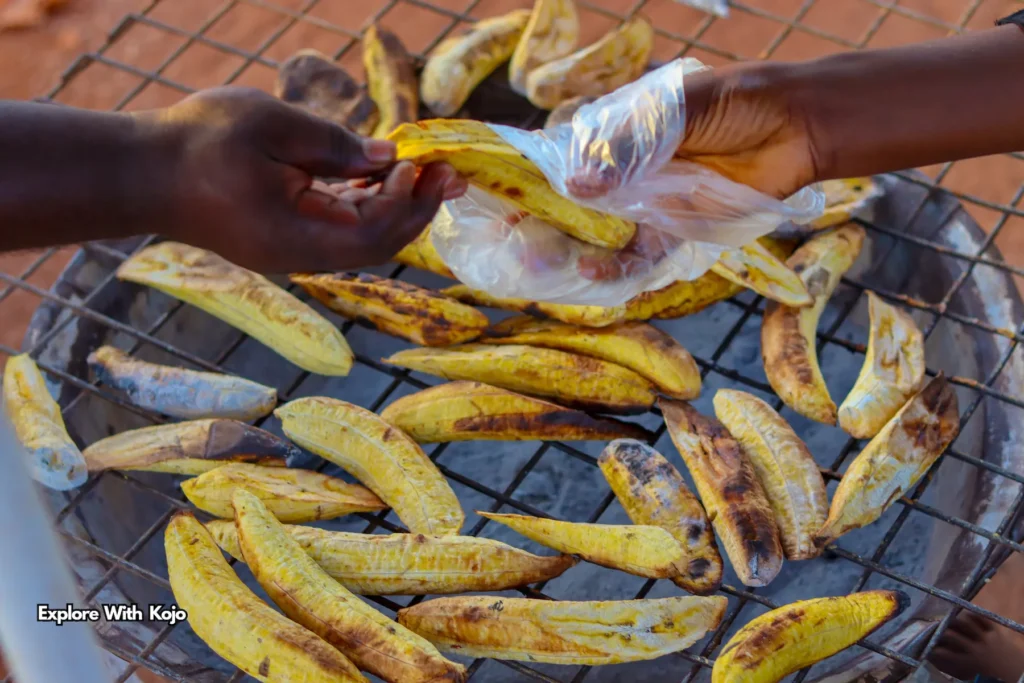 Hands exchanging roasted plantain on a grill in Ghana