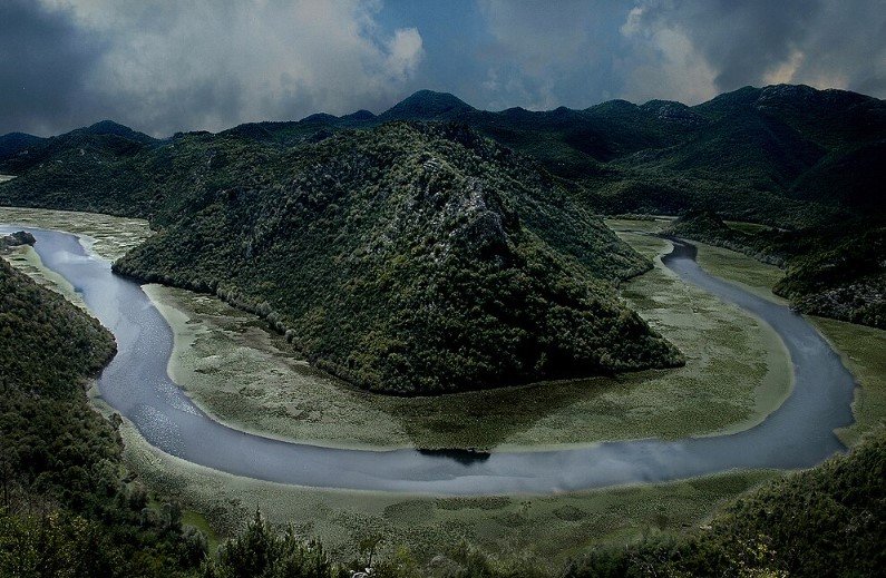Shkodër Lake in Albania with mountains reflecting on calm water.