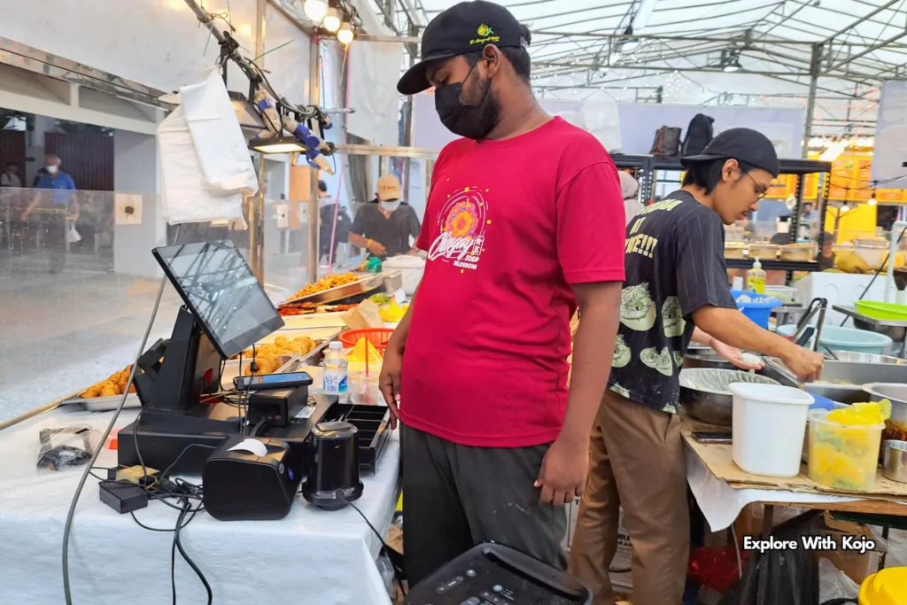 Vendor operating a cashier at a Pasar Malam food stall.
