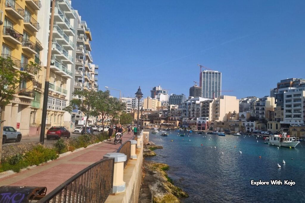 St Julian’s waterfront promenade along Spinola Bay in Malta, with apartments, boats, and clear blue water.