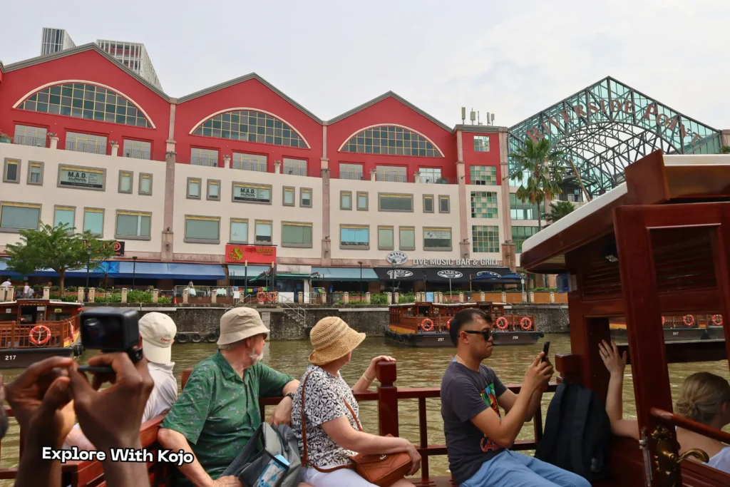 People enjoying the Singapore River Cruise, passing Riverside Point and Clarke Quay’s colorful waterfront buildings.