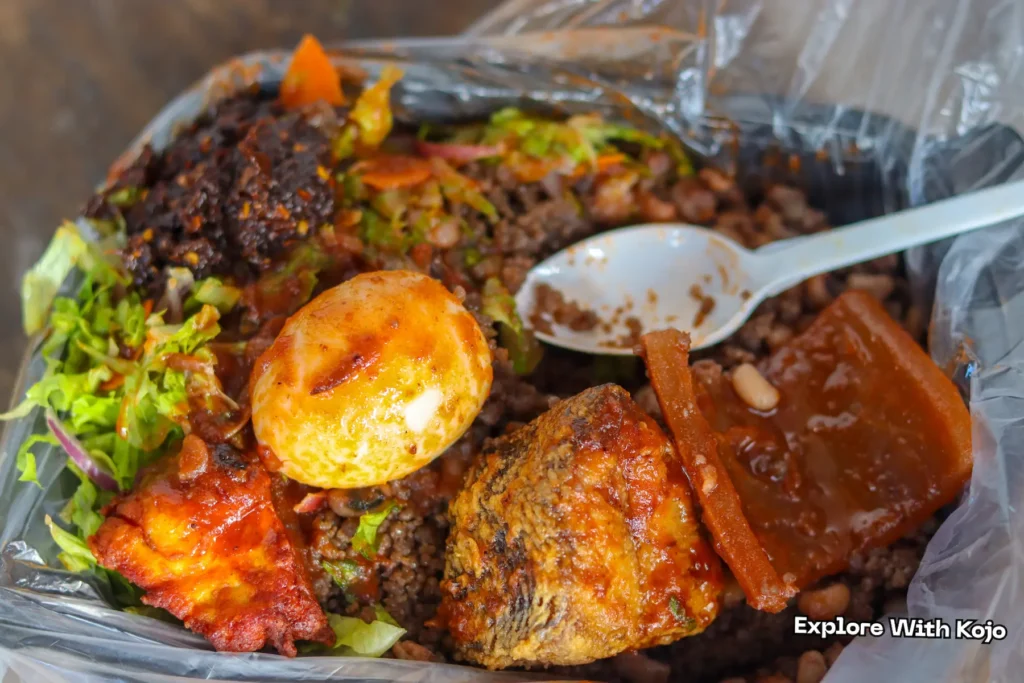 Wasawasa with fried fish, boiled egg, and salad in a black food container.