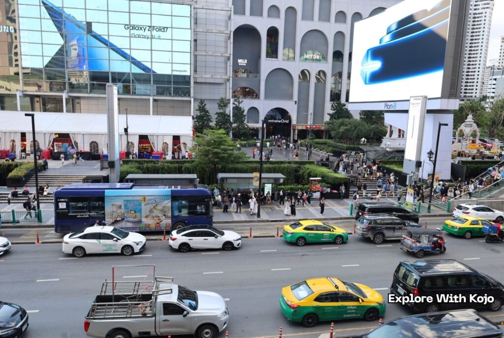 Busy Bangkok street in front of CentralWorld with taxis, tuk-tuks, and buses moving through traffic