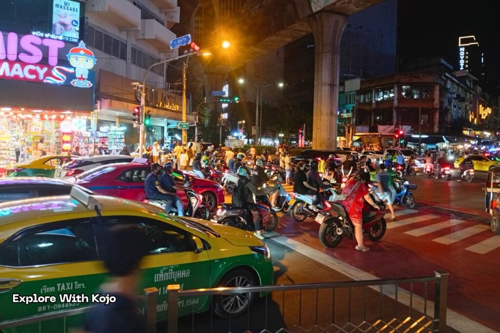 Crowded Bangkok traffic with motorbikes and taxis outside Nana Plaza at night.