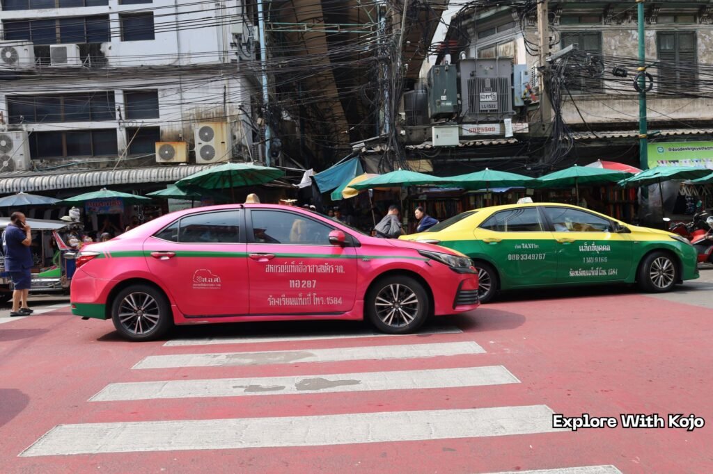 Pink and yellow-green taxis at a busy Bangkok street crossing near local markets