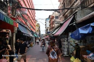 Busy Bangkok market street with vendors and pedestrians, showing the lively city atmosphere before traveling to nearby beaches.