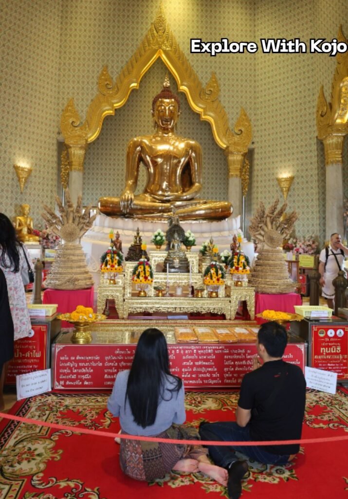 Visitors sitting respectfully on the floor in front of the Golden Buddha inside a Bangkok temple, following proper temple etiquette during worship.