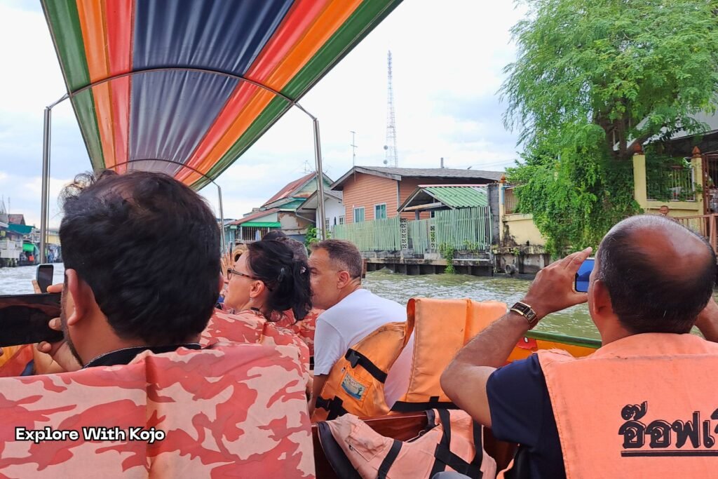 Tourists riding a longtail boat on the Chao Phraya River, passing riverside homes in Bangkok.