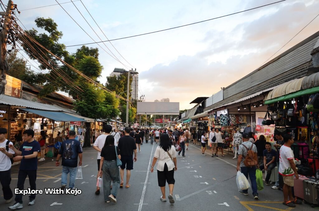 Shoppers walking through an open street at Chatuchak Weekend Market during the late afternoon.