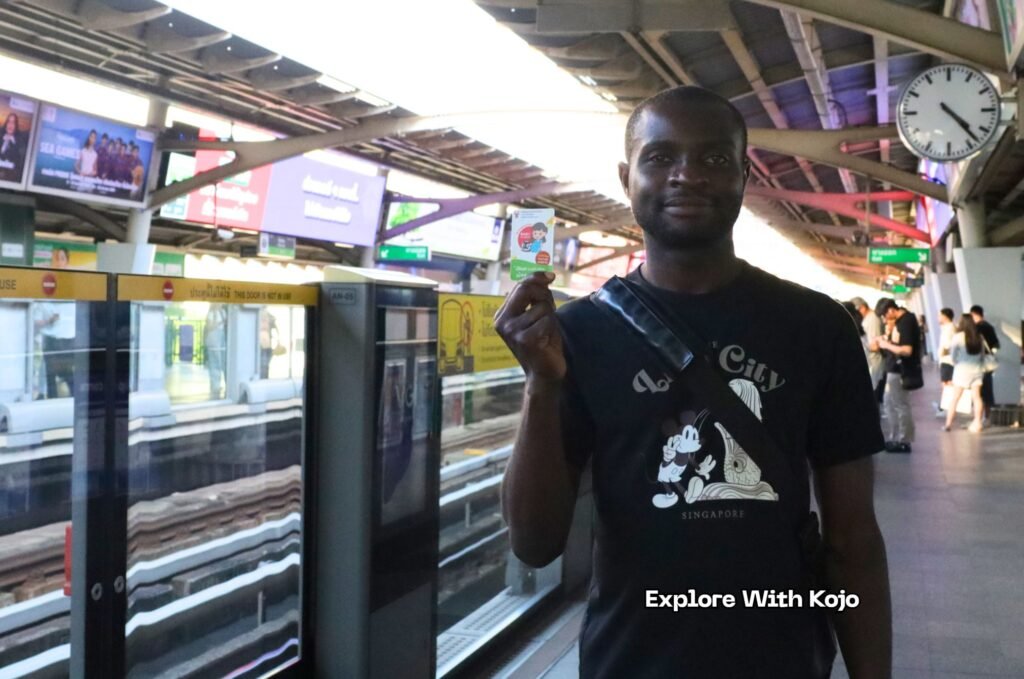 Kojo standing at a BTS Skytrain station in Bangkok holding his train ticket before heading to Chatuchak Weekend Market.