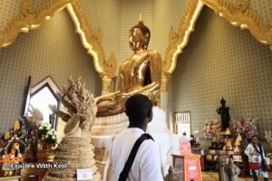 Kojo standing inside Wat Traimit in front of the Golden Buddha statue.