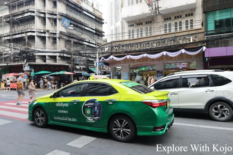 Green and yellow taxi driving through Bangkok.