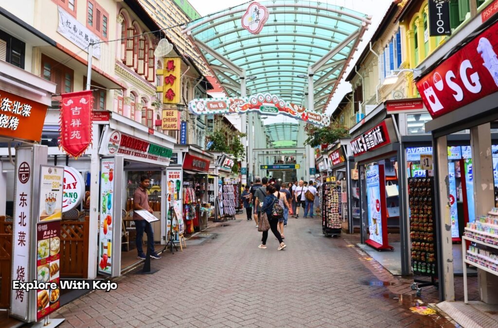 Street market in Singapore’s Chinatown with shops, food stalls, souvenir stands, and people walking through.