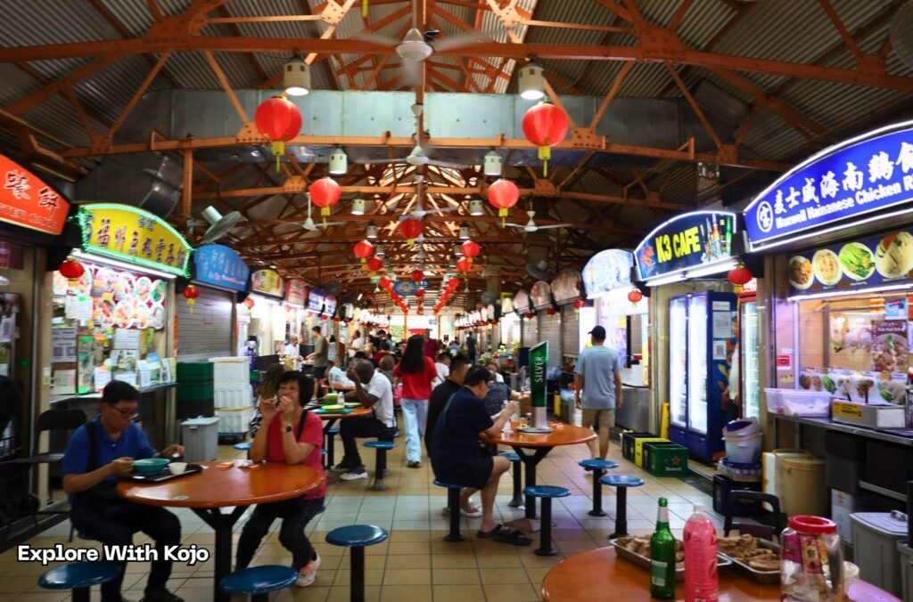 Inside Maxwell Food Centre in Singapore’s Chinatown with hawker stalls and people eating local food. 