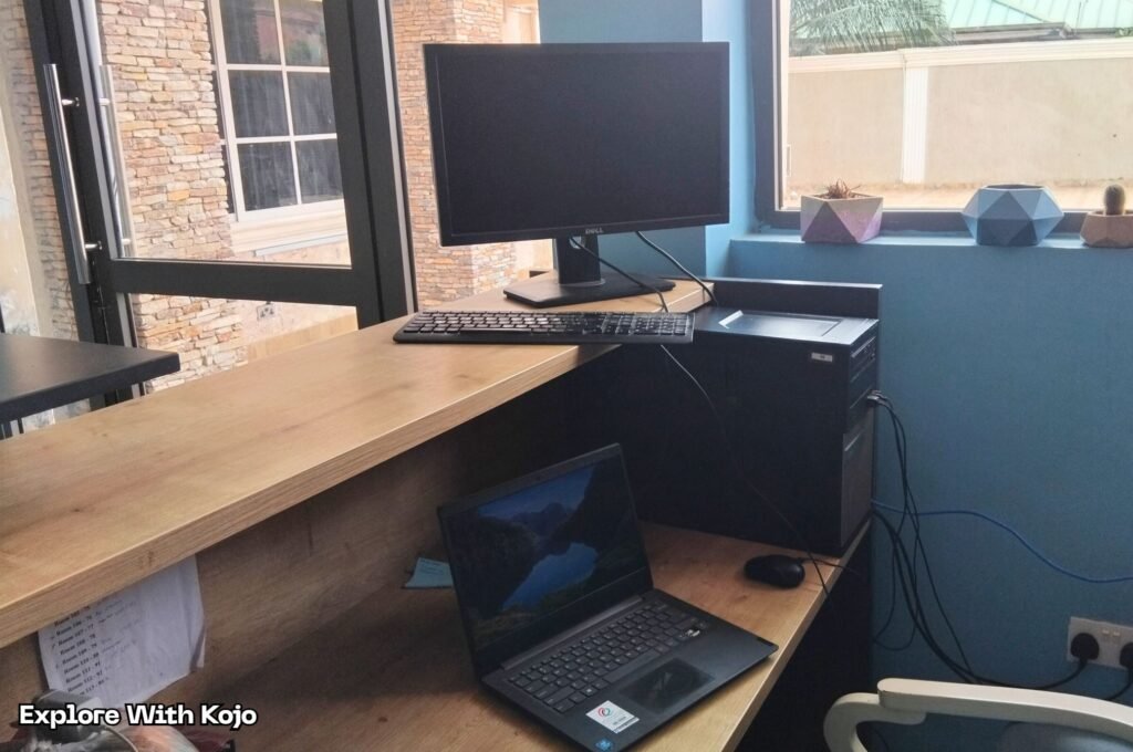 Simple remote work setup in Ghana with a laptop, monitor, and keyboard at a small office desk.